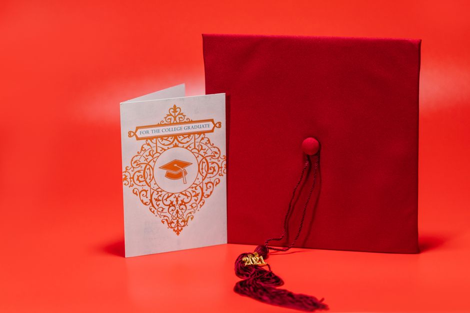 A stylish graduation card and red mortarboard on a vibrant red background.