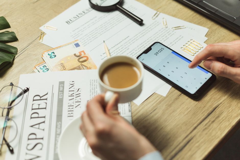 High-angle view of a business workspace with documents, coffee, currency, and smartphone calculator.