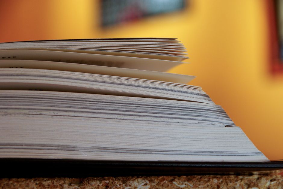 A close-up view of an open book with pages turning, set against a warm background.